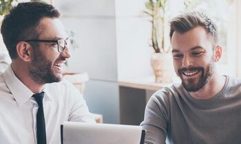 two men in an office looking at a screen and smiling